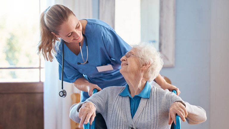 Eine häusliche Pflegekraft und eine ältere Frau mit einer Behinderung im Rollstuhl in einer medizinischen Pflegeeinrichtung.