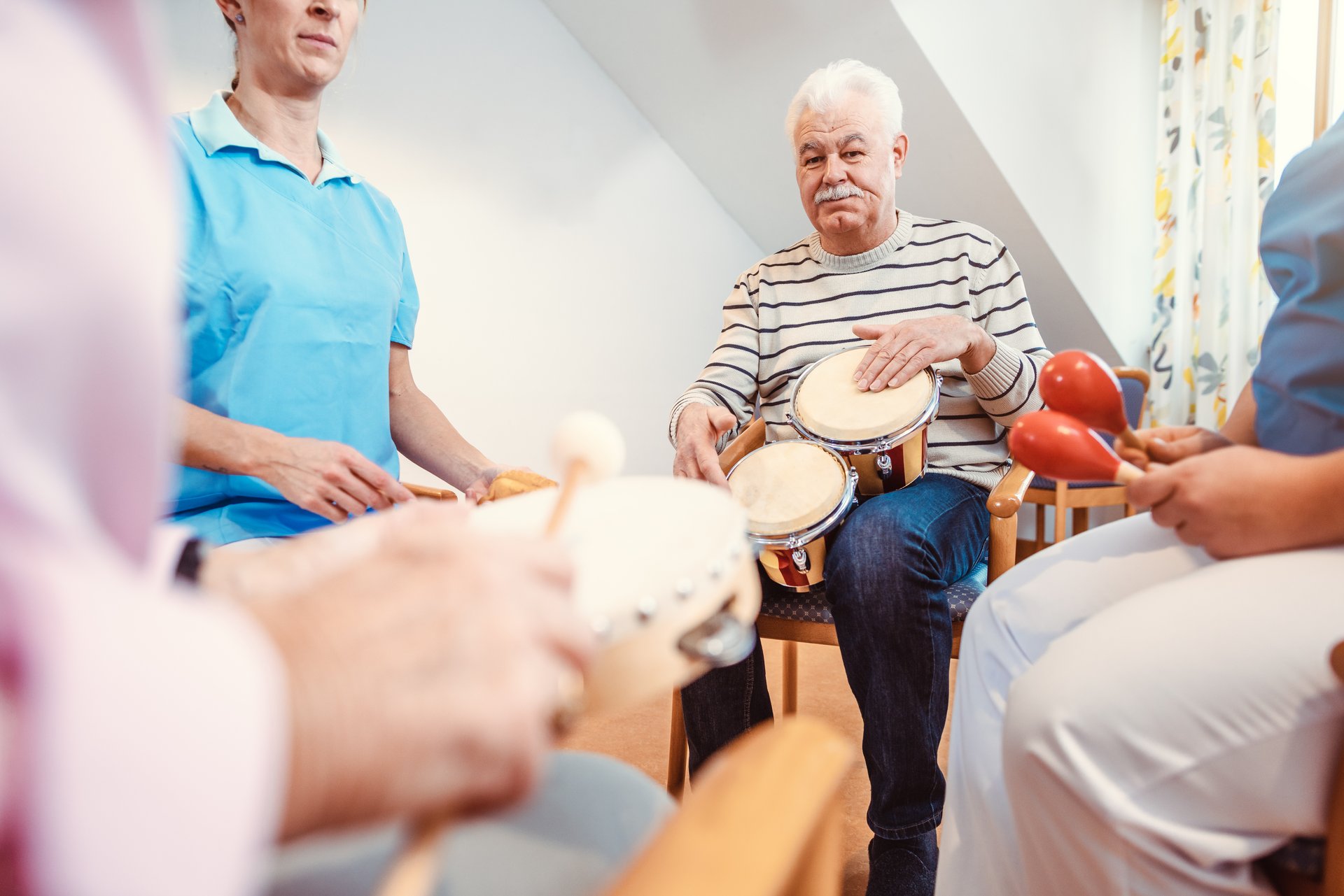 Senioren im Pflegeheim musizieren mit Rhythmusinstrumenten als Musiktherapie.